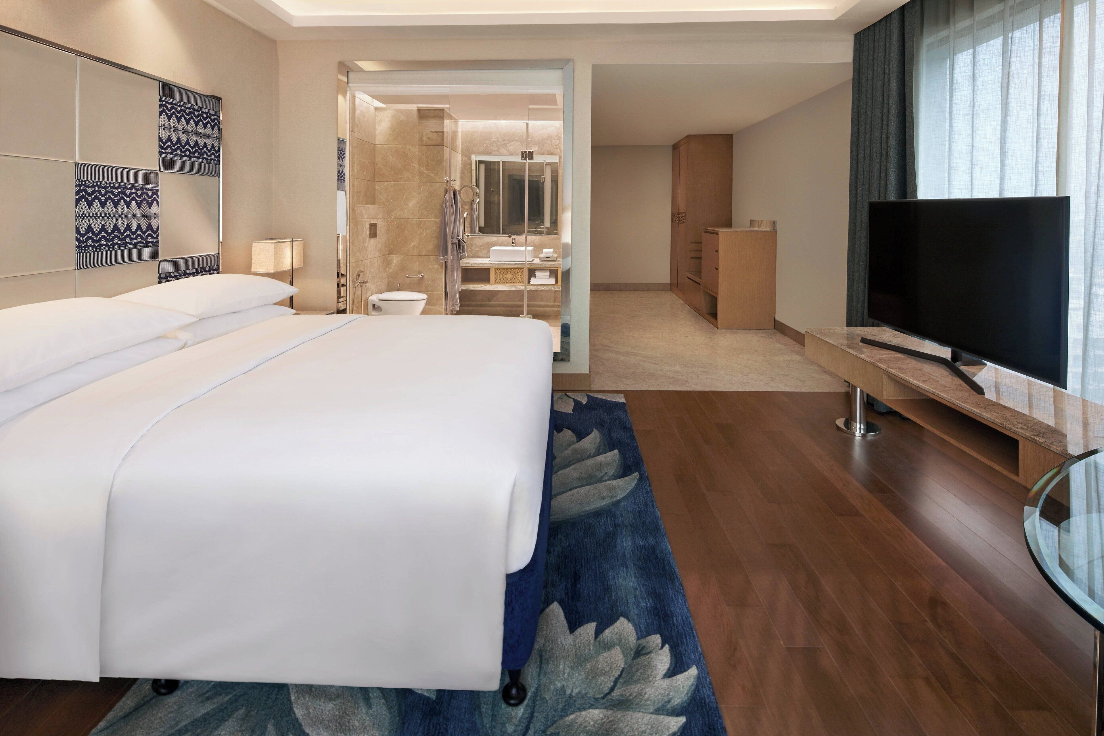 A modern hotel room with a large bed, a TV, a bathroom with a shower, and a walk-in closet.