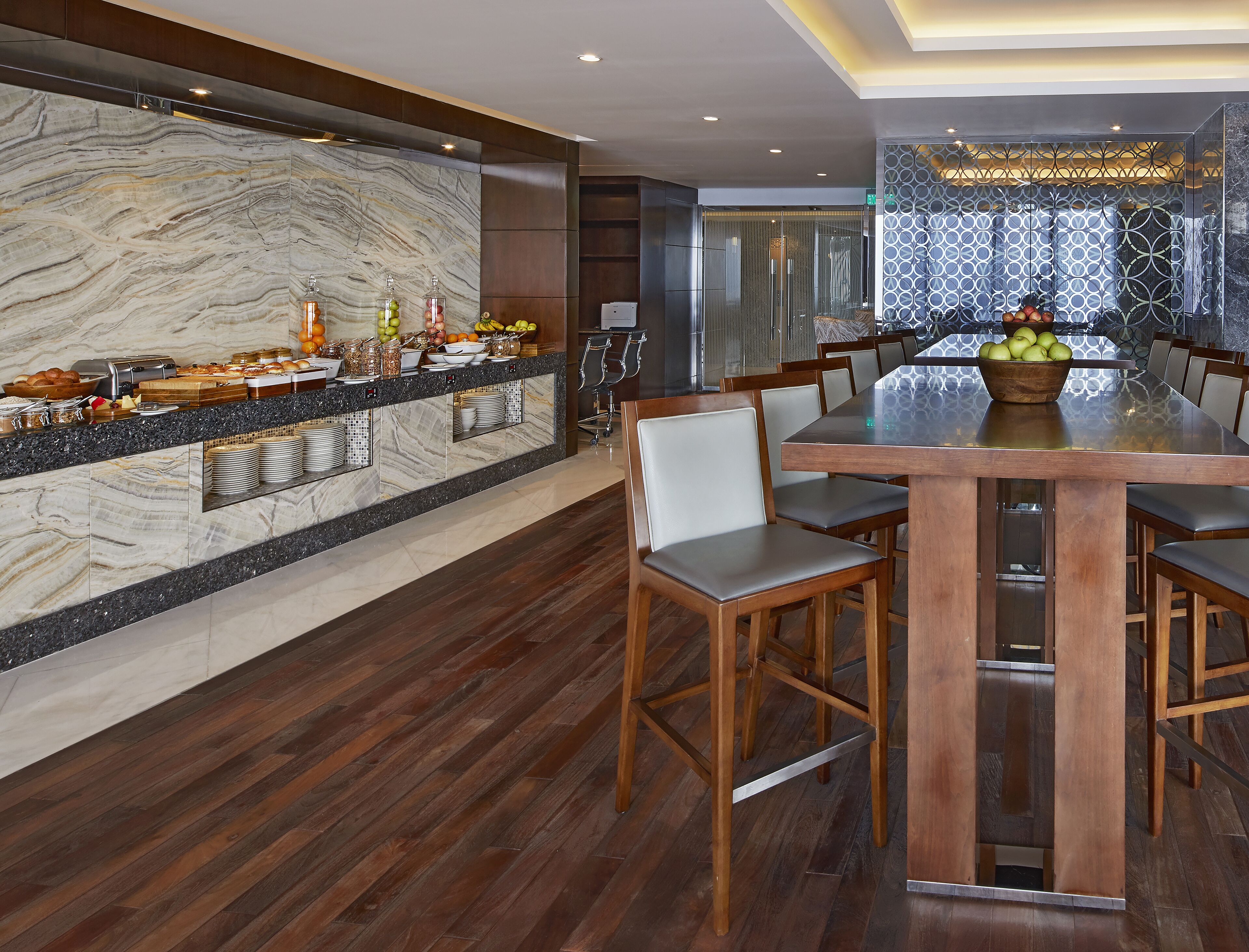 A modern dining area with a marble backsplash, wooden chairs, and a buffet with various food items.