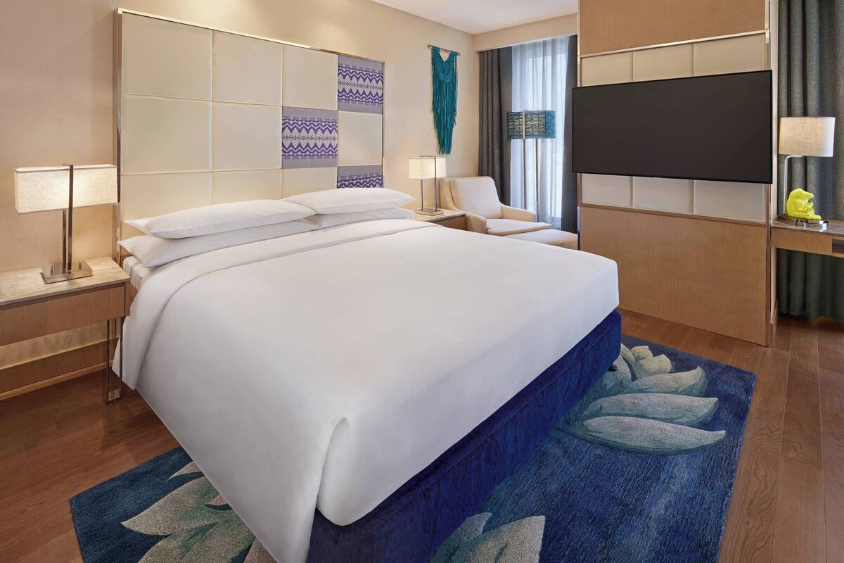 A hotel room with a large bed, a flat-screen TV, a desk, and a chair.