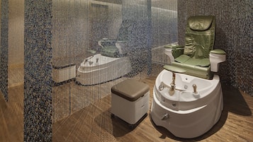 Experience the unique bathroom with a textured mosaic wall, a green massage chair, and a pedestal sink with a curved basin and multiple faucets.