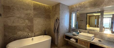 A modern bathroom with a freestanding bathtub, a large mirror, and marble walls.