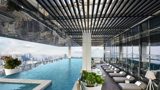 Ein Rooftop-Endlospool mit Blick auf die Stadt, eine Lounge mit Sitzgelegenheiten und Topfpflanzen.