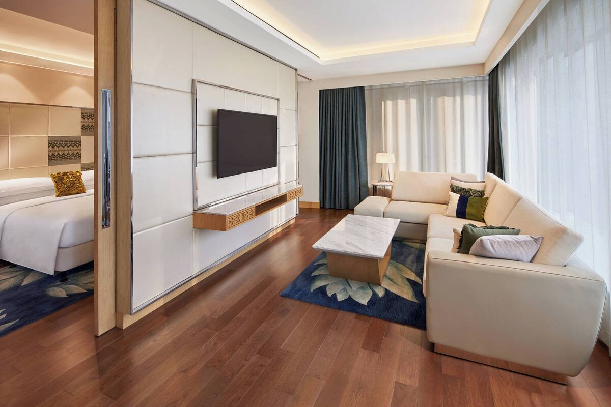 A modern hotel room with a large bed, a sofa, a coffee table, and a TV mounted on the wall.