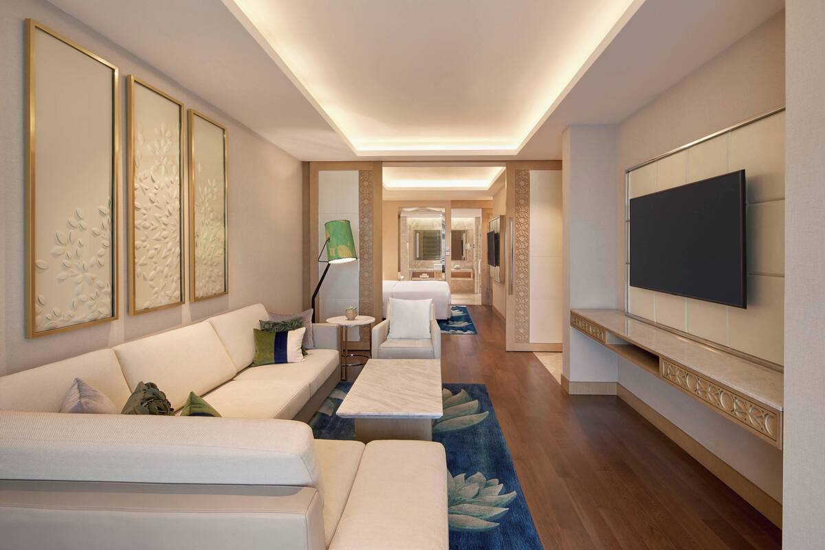 A modern hotel room with a sofa, a coffee table, and a TV mounted on the wall.