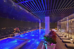 Une piscine à débordement située sur le toit, dotée d’un éclairage bleu, de chaises longues et offrant une vue sur la ville.