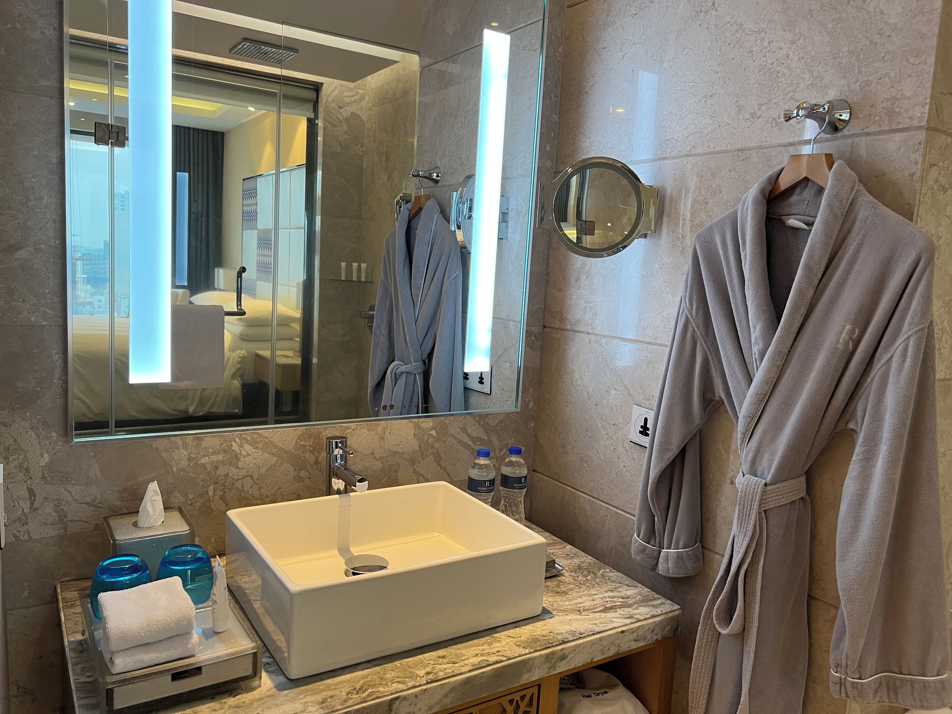 Un baño moderno con un espejo grande, un lavamanos blanco y una bata colgada en un perchero.