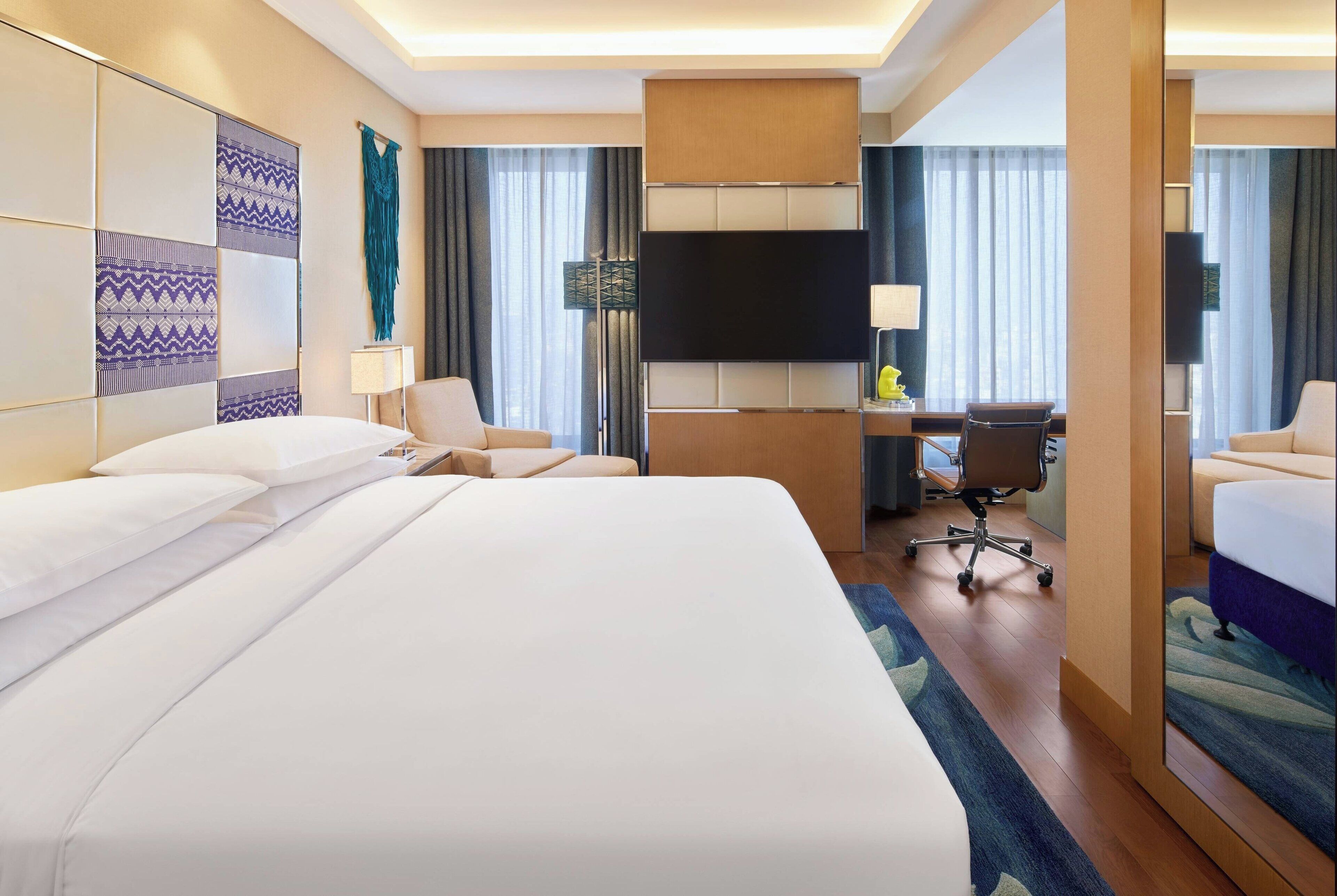 Habitación de hotel con una cama grande, un escritorio, una silla, un televisor de pantalla plana y un espejo.