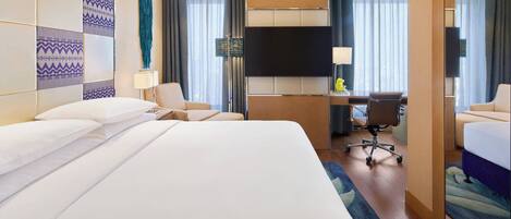 Habitación de hotel con una cama grande, un escritorio, una silla, un televisor de pantalla plana y un espejo.