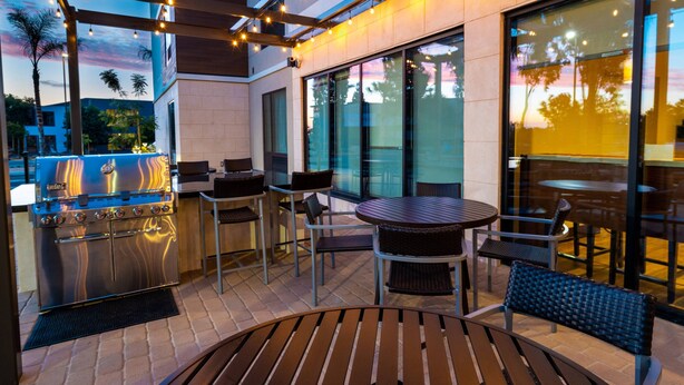 Un espace extérieur aménagé en terrasse, avec un barbecue, des sièges et de grandes fenêtres.