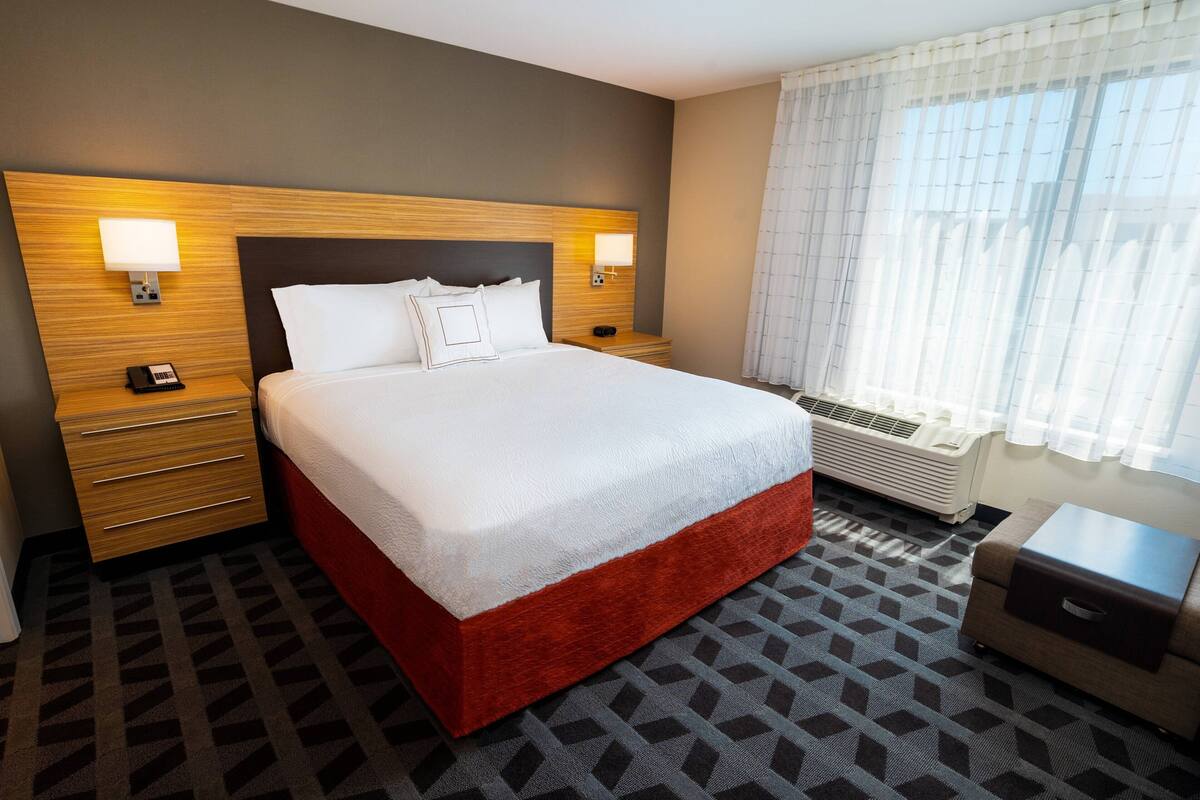 Een hotelkamer met een groot bed, twee nachtkastjes met lampen, een verwarming en een klein tafeltje met lade.