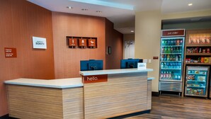 Un comptoir d’accueil d’hôtel avec une pancarte indiquant « bonjour », une autre indiquant « enregistrement » et « départ », et une troisième indiquant « détente » au-dessus d’un réfrigérateur à boissons.