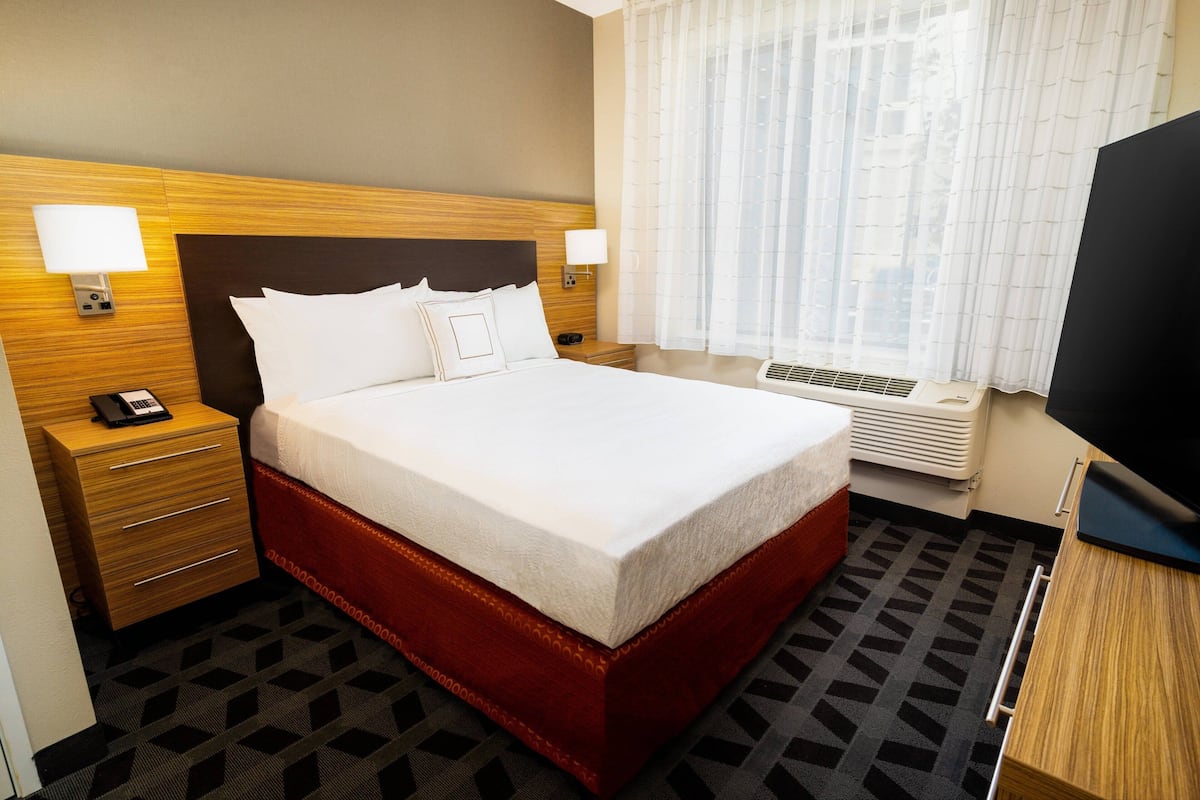 Hotelkamer met een groot bed, houten hoofdeinde, bedlampjes, een bureau met telefoon en een televisie.
