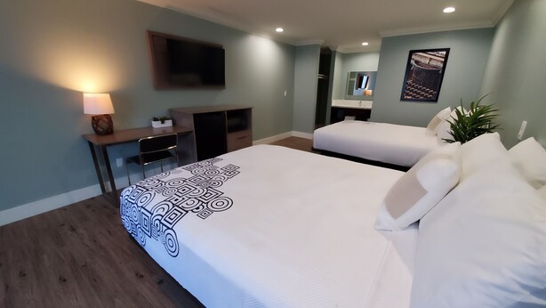Ein Hotelzimmer mit einem großen Bett, einem Schreibtisch, einem Sessel, einem an der Wand befestigten Fernseher und einer kleinen Pflanze.