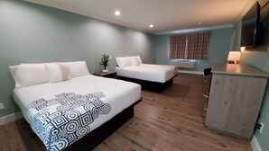 A hotel room with two beds, a desk, a chair, a potted plant, and a window with blinds.