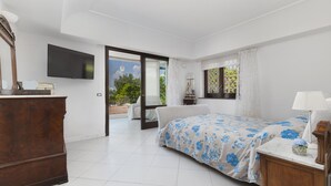 A bedroom with a bed, dresser, TV, and a view of the outdoors.