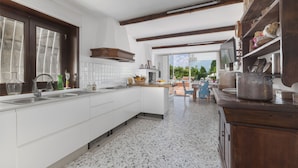 A modern kitchen with white cabinetry, a large island, and wooden beams on the ceiling.