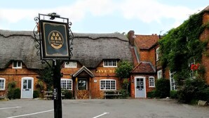 Un pub traditionnel avec un toit de chaume et des murs en briques, une enseigne et un espace de stationnement à l’avant.