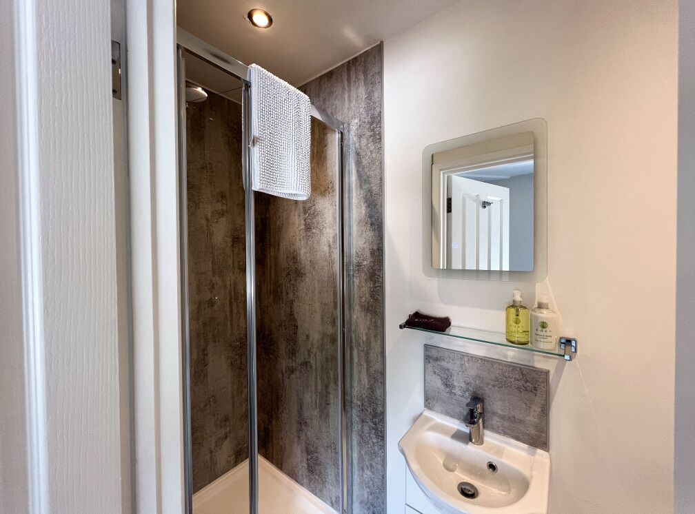 A bathroom with a glass shower enclosure, a sink with a marble countertop, and a mirror above the sink.