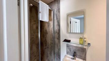 A bathroom with a glass shower enclosure, a sink with a marble countertop, and a mirror above the sink.