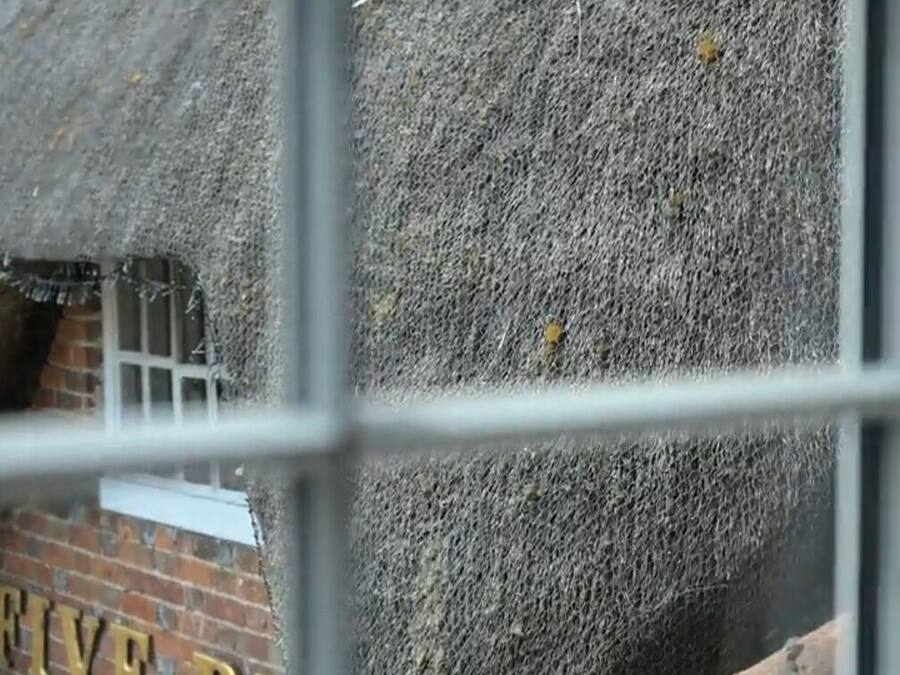 A window view of a brick building with a thatched roof and a visible sign with the letters "FIVE".