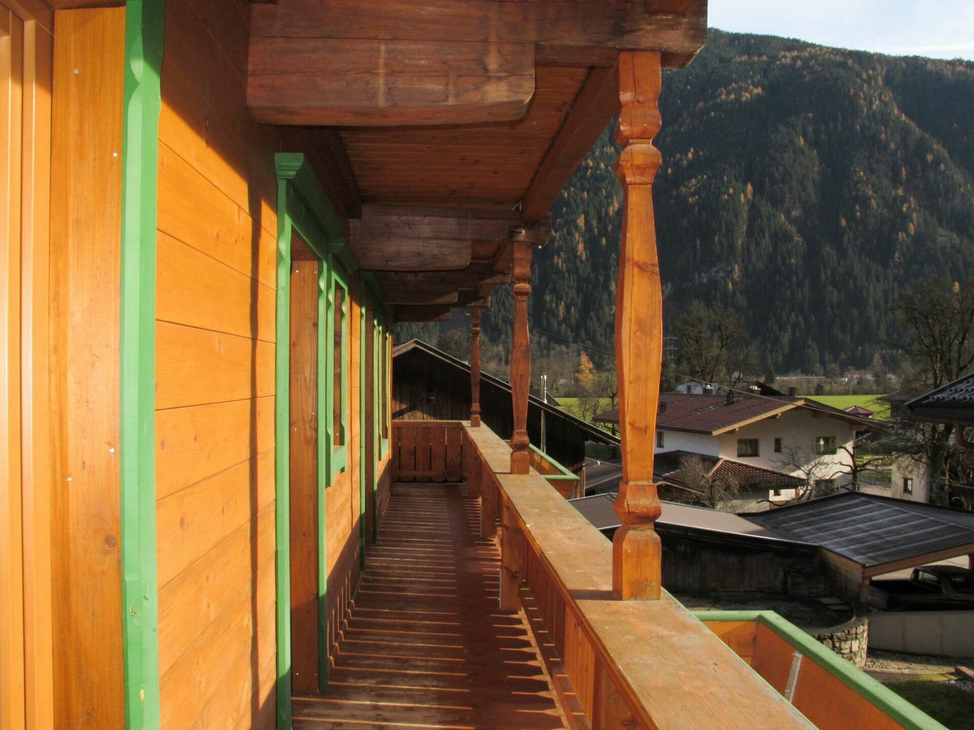 A wooden balcony with a view of houses and mountains in the background.