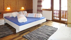 Un dormitorio con techo de madera, una cama con ropa de cama azul, dos lámparas de noche, una ventana con cortina y suelo de madera.