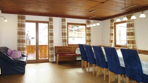 Una habitación con techo de madera, un sofá, un banco y una zona de comedor con sillas y una mesa.