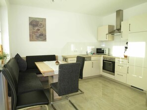 A modern kitchen with white cabinets, a microwave, and a stove. There is a dining area with a table and chairs.