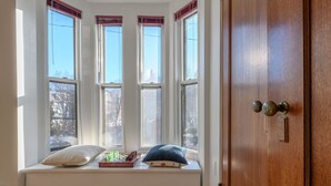 A room with a bay window seating area, a wooden door, and a view of the outside.