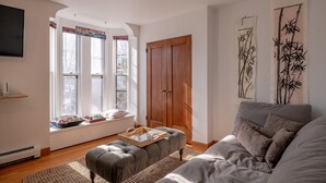 A living room with a grey sofa, a wooden wardrobe, and a window with a view.