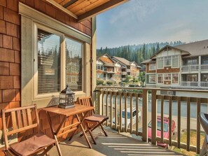 A wooden balcony with a table and chairs, overlooking a lake and a row of houses.