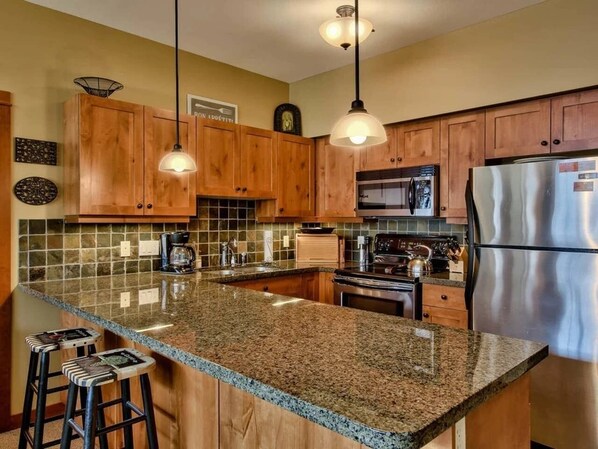 A kitchen with wooden cabinets, granite countertops, stainless steel appliances, and pendant lighting.