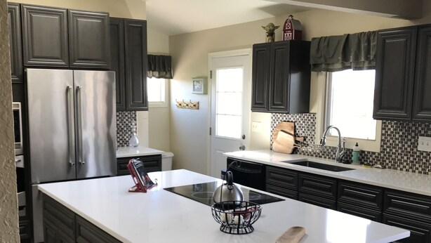 A modern kitchen with dark cabinetry, a large island, stainless steel appliances, and a checkered backsplash. - A Spacious Home With Great Views & Wildlife (Parker)