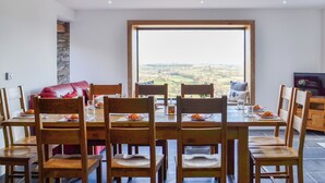 Un espace repas comprenant une grande table et des chaises, un mur en pierre et une vue sur la campagne.