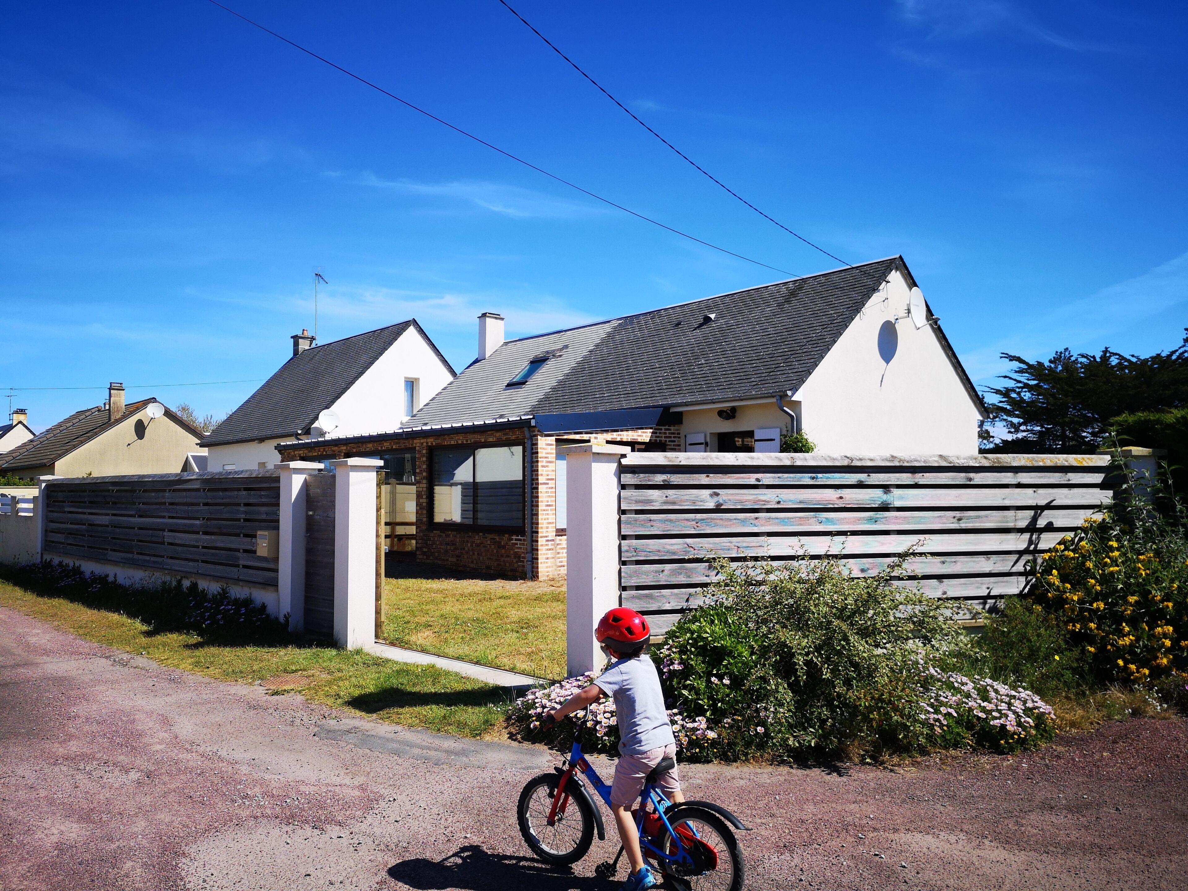 A residential area with houses, a child on a bicycle, and a clear blue sky.