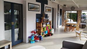 A spacious room with a large table and chairs, a bookshelf with various items, and a sliding glass door leading to an outdoor area.