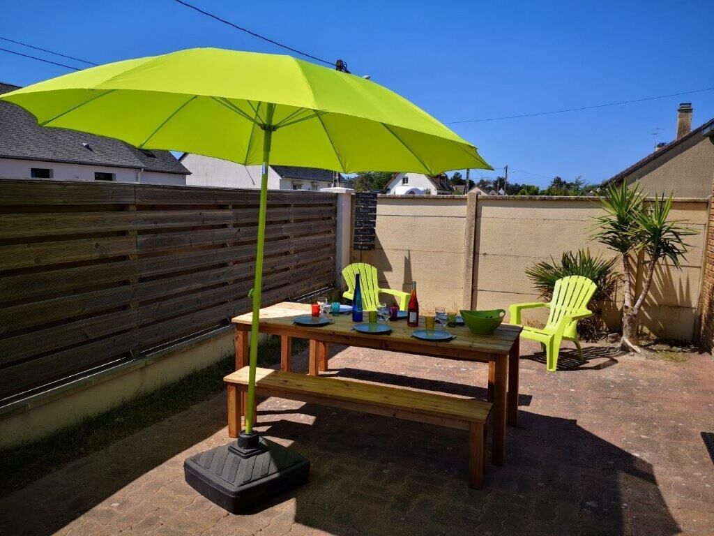 Un patio al aire libre con una mesa de madera, bancos y un paraguas verde brillante.