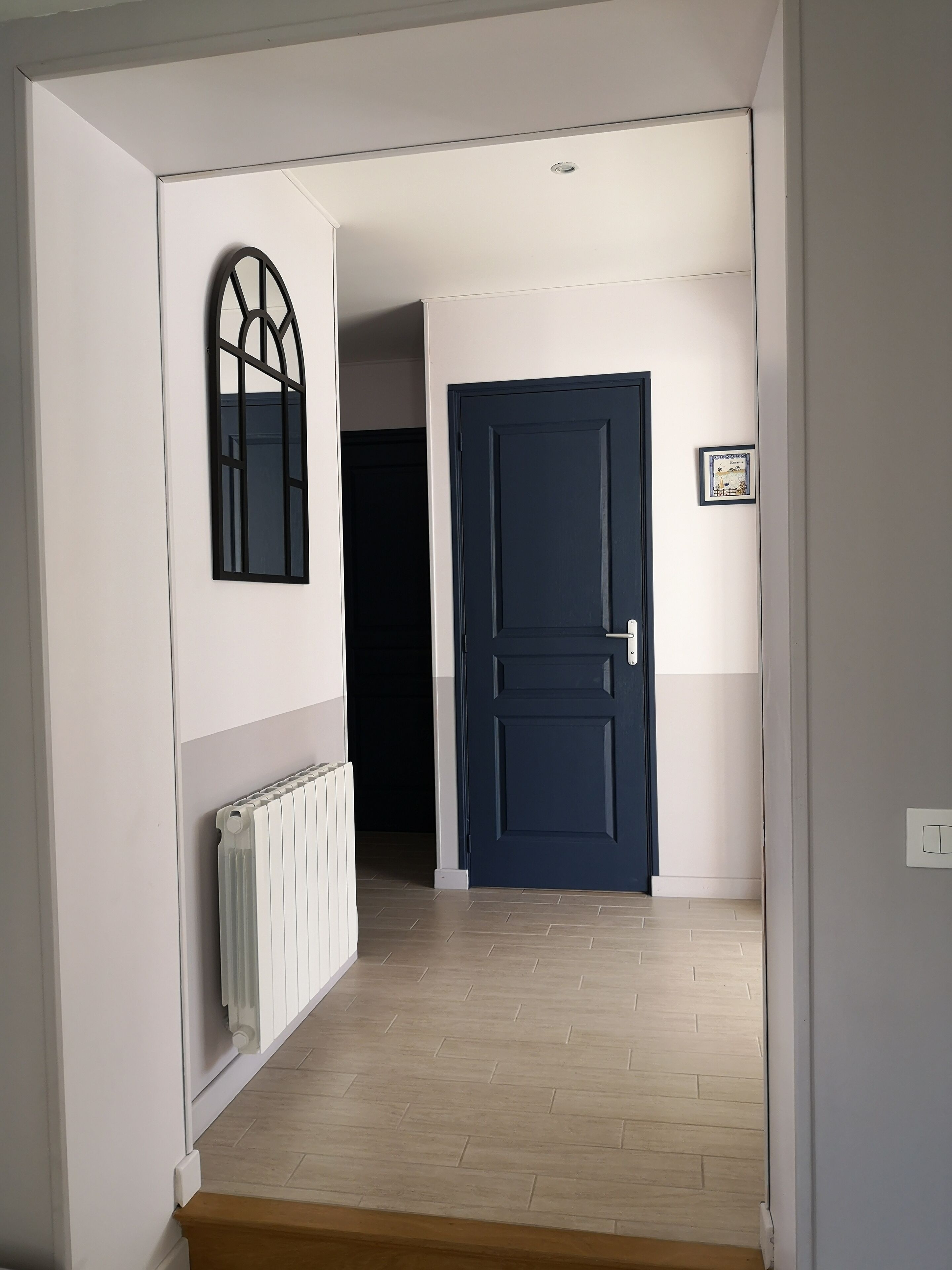 A hallway with a white radiator, a dark blue door, and a framed picture on the wall.