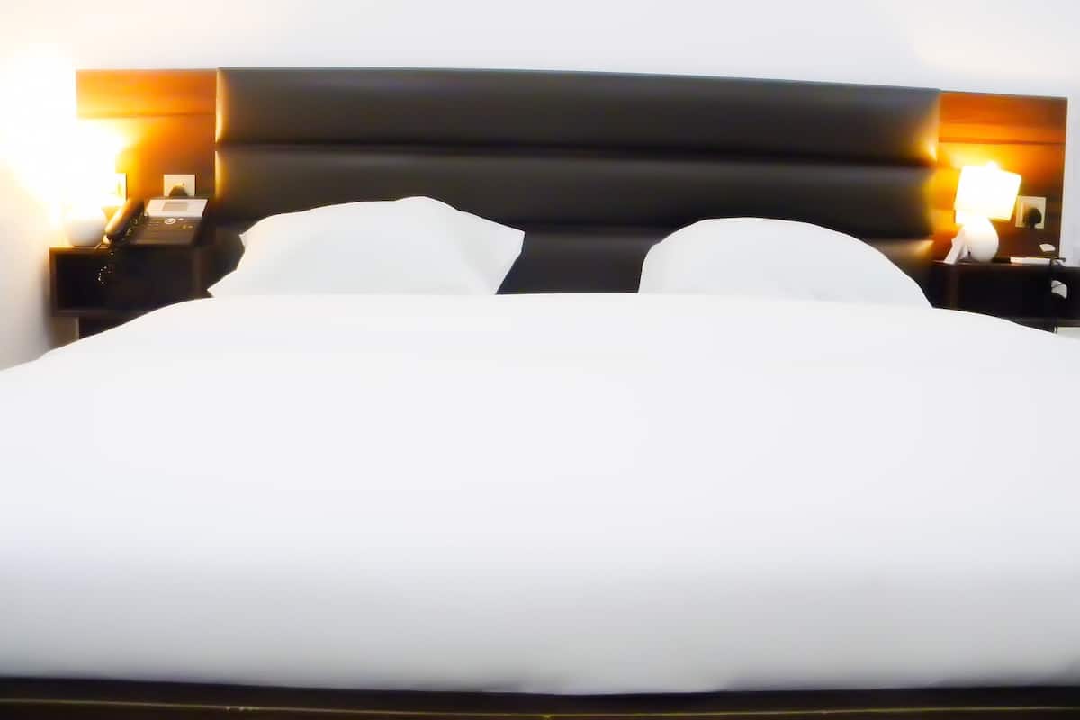 A neatly made bed with white linens, a dark headboard, and two bedside lamps on either side.
