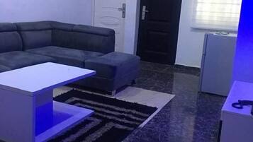 Een moderne woonkamer met een hoekbank, een klein witte tafel en een donkere marmeren vloer.