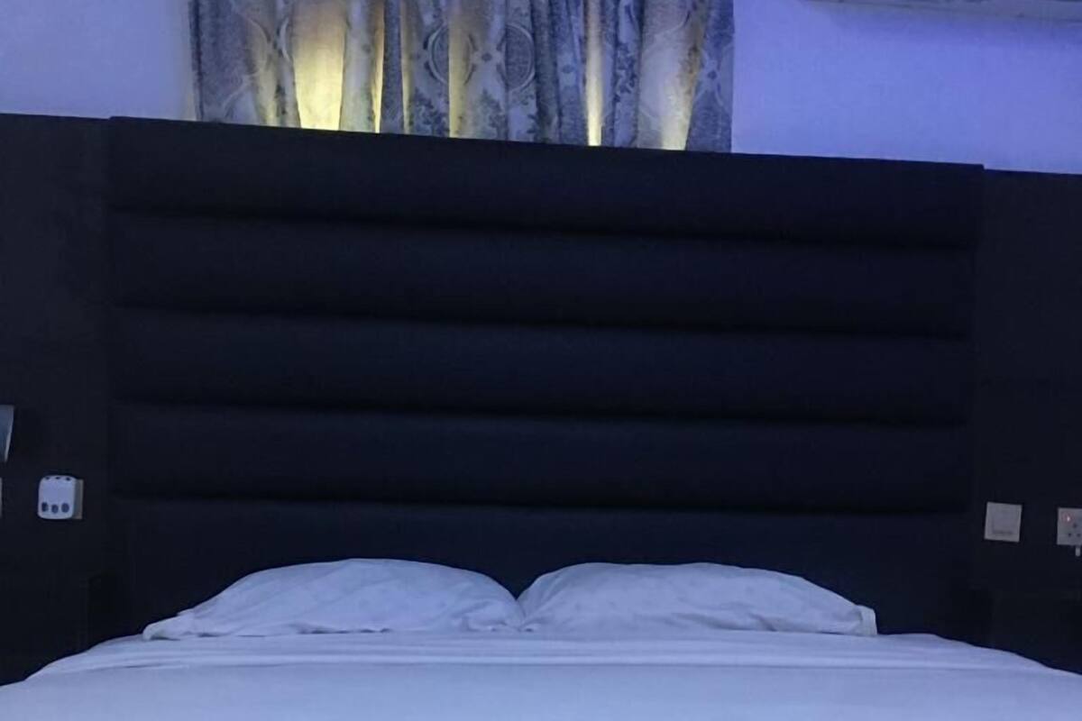 A bed with white bedding, a dark headboard, and an air conditioning unit on the wall.