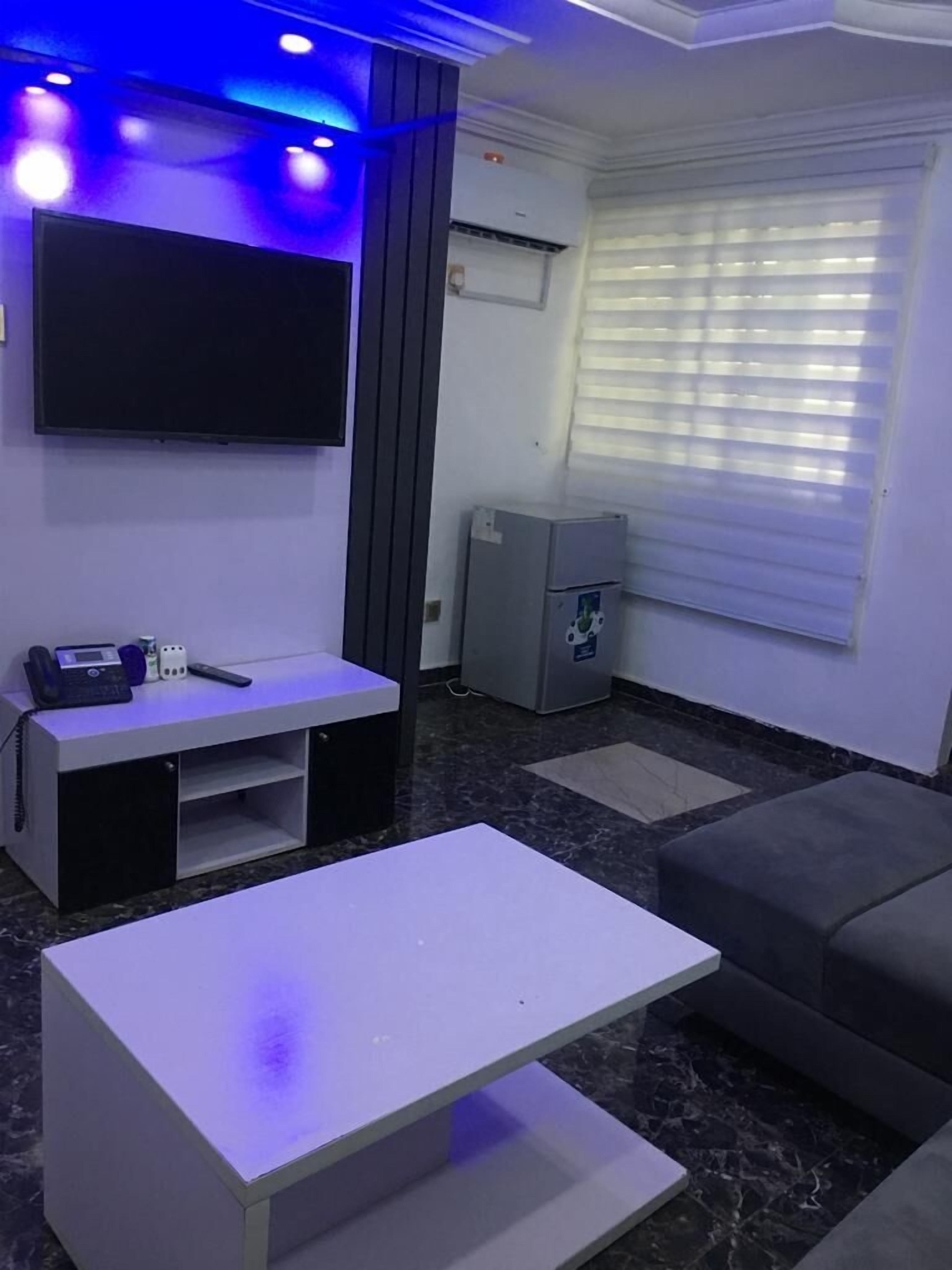 Un salon moderne avec un téléviseur à écran plat, un petit meuble de rangement pour les appareils multimédias, un canapé gris et une table basse blanche.