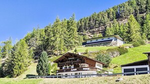 Ein traditionelles Holzchalet mit Balkon, vor einer Berglandschaft und dichtem Wald gelegen.