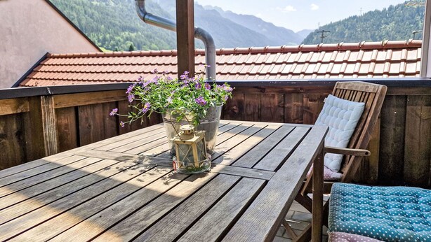 A wooden deck with a table and chairs, a potted plant, and a view of mountains. - Nice apartment for 8 people with WIFI, TV and balcony (Prutz)