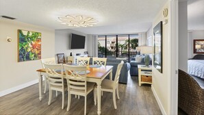 Un salon moderne comprenant un coin repas, un téléviseur à écran plat et une grande fenêtre donnant sur un quartier résidentiel.