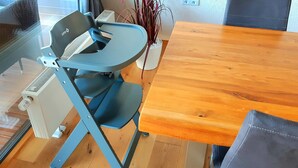 A room with a wooden dining table, a blue folding chair, and a white vase with plants.