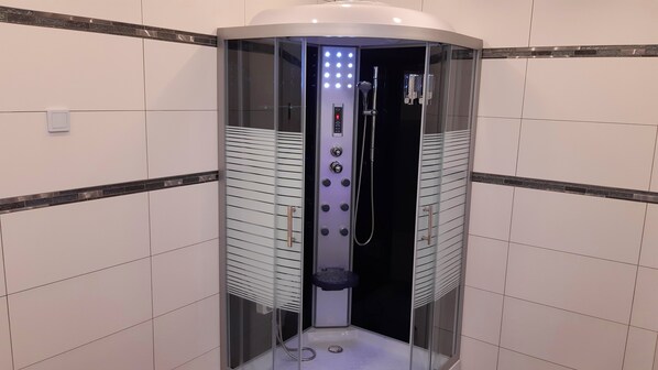 Een moderne, afgesloten douchecabine met bedieningspaneel, glazen deuren en een betegelde vloer.