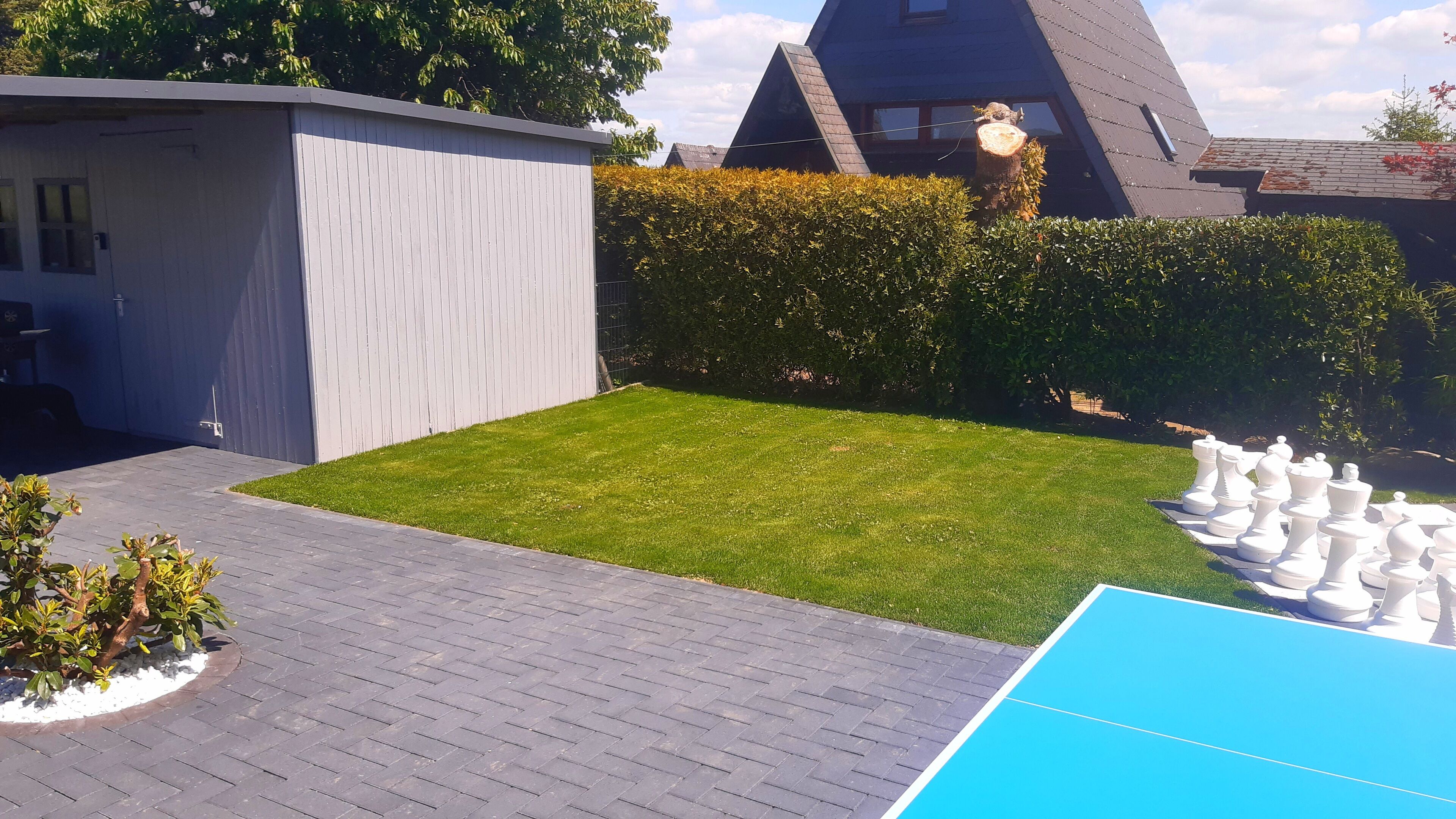 A modern outdoor area with a neatly trimmed lawn, a brick patio, and a blue play area.