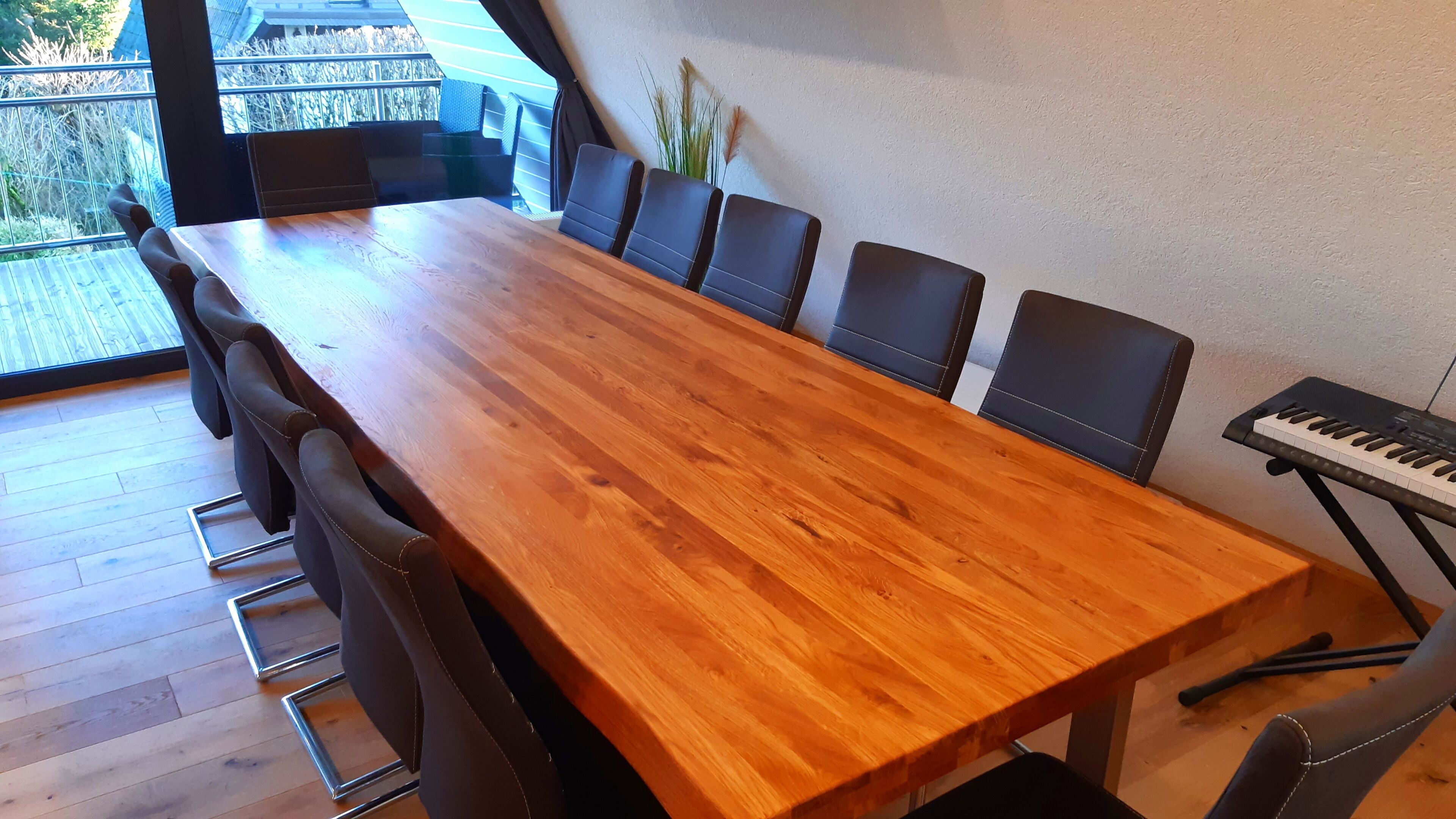 Ein Holztisch mit sechs Stühlen, einer Tastatur und Blick auf einen Balkon mit Pflanzen.