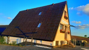 A building with a sloped roof, a small window, and a sign that reads "Dem Himmel so nah".